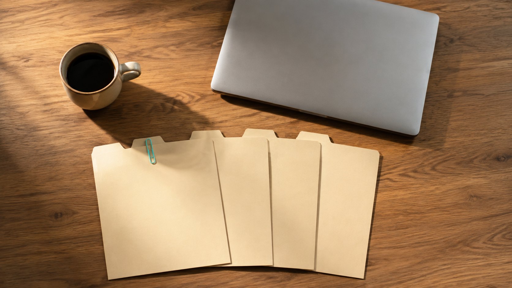 Five manila file tabs fanned out on a wooden desk beside a closed laptop